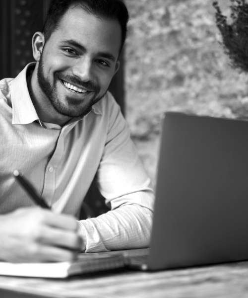 man smiling at computer with pen and paper